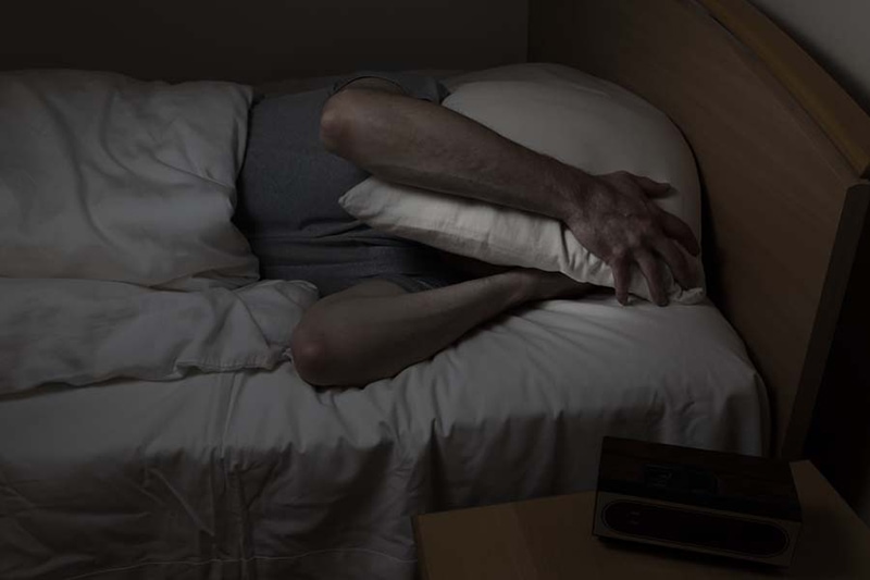 Mature man, with pillow covering entire face, cannot sleep at night from insomnia