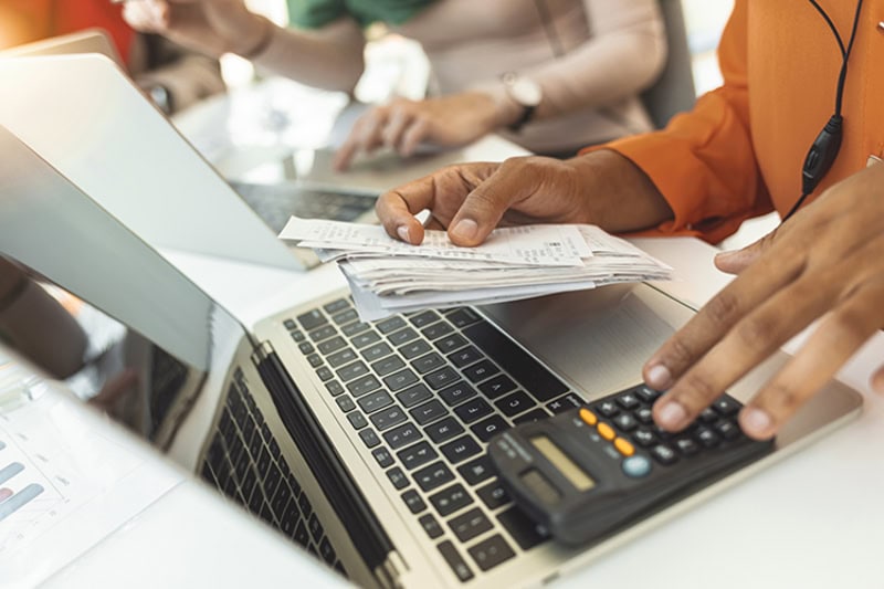 Table full with papers invoices cheque bills, female hands holding receipt calculating company expenses results of incomes, bookkeeper accountant doing paperwork concept.