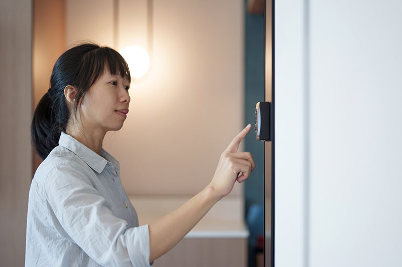 A women at home adjusts the temperature using a smart thermostat, exemplifying smart home concepts.