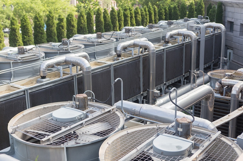 commercial heat pump units on the roof of a commercial building on a sunny day with some green trees in the background