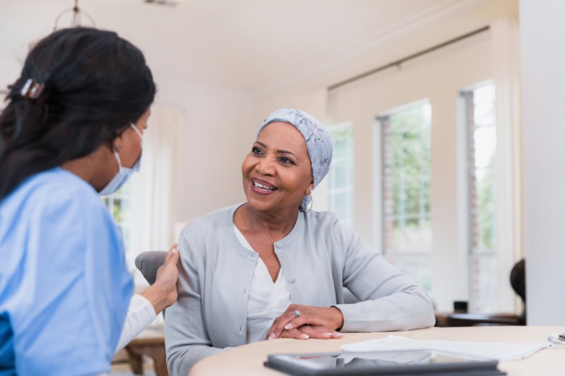 The compassionate female nurse listens to the senior adult female cancer patient during a home visit.