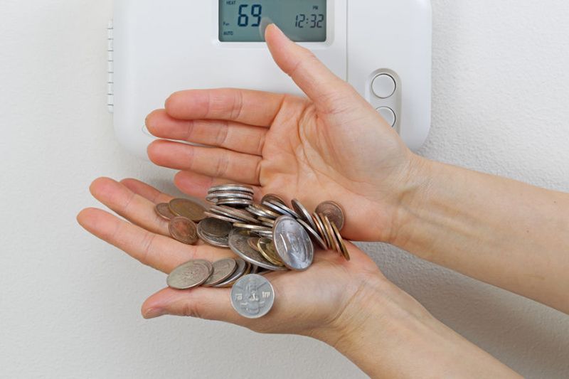 Coins in hands by a thermostat.