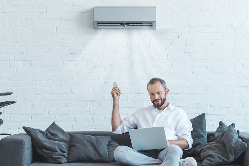 4 Amazing Benefits of Ductless Units. Man sitting on his couch turning on his ductless system.