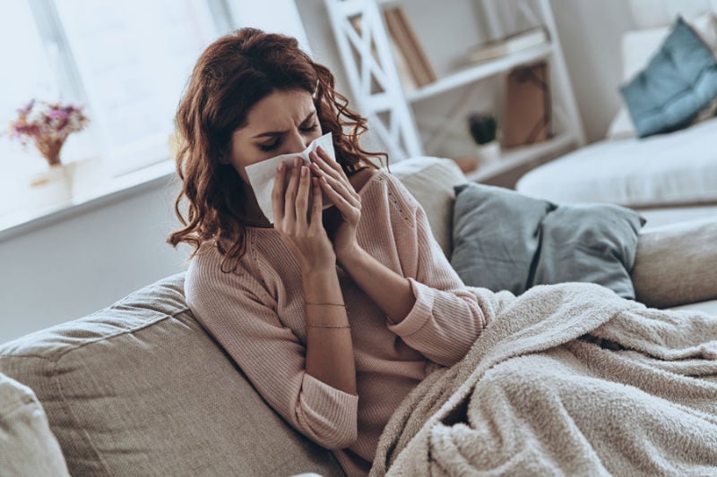 Top view of sick young women blowing her nose using facial tissues while sitting on the sofa at home